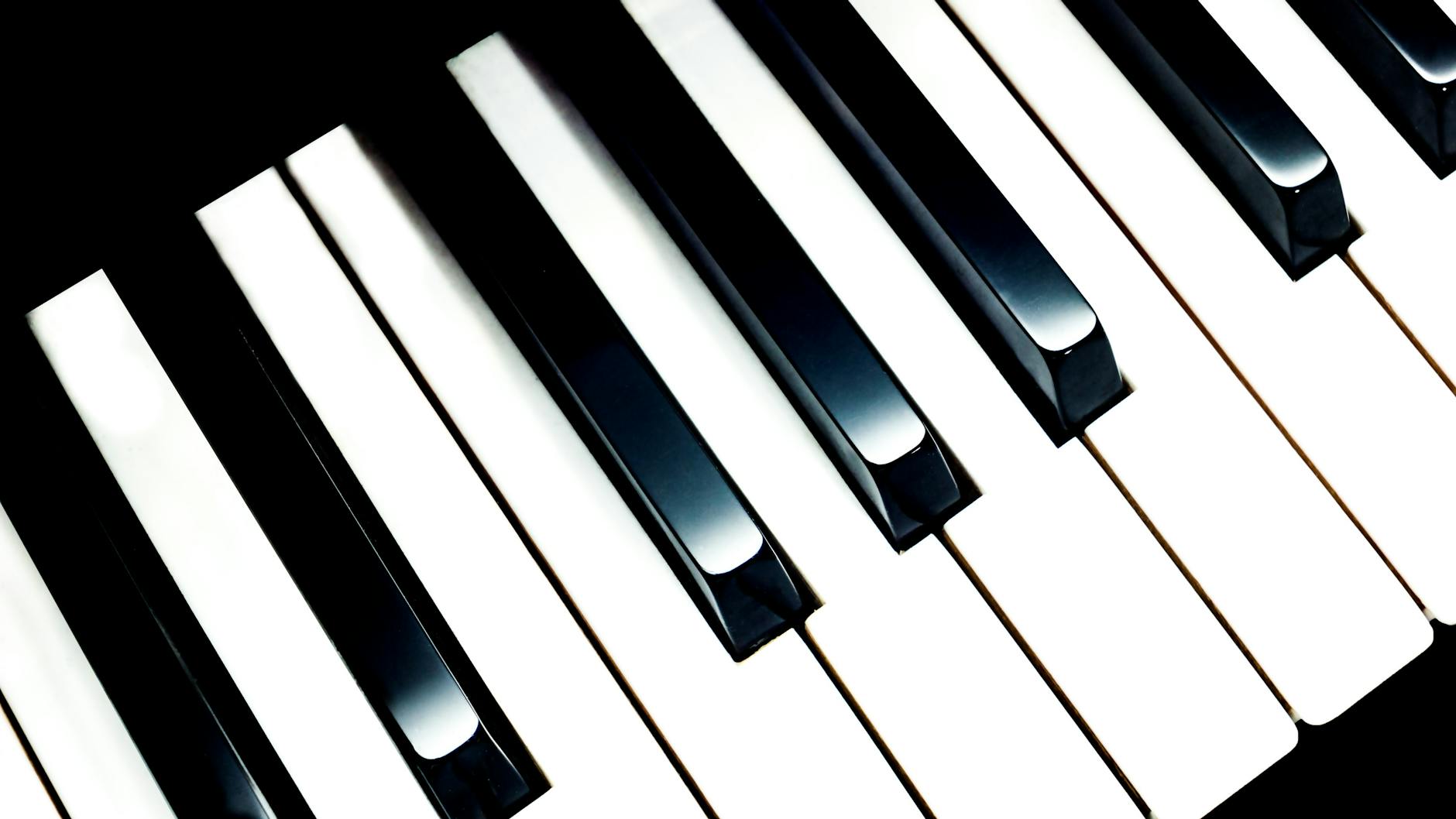 A high-angle, close-up shot of a piano keyboard, showcasing the black and white keys in a diagonal composition. The lighting highlights the glossy surfaces of the keys.